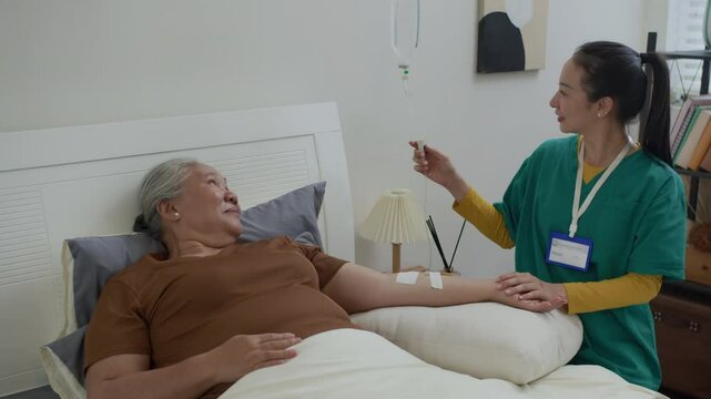 Young female physician helping Asian senior lady in receiving IV drip infusion and vitamin therapy while providing home service