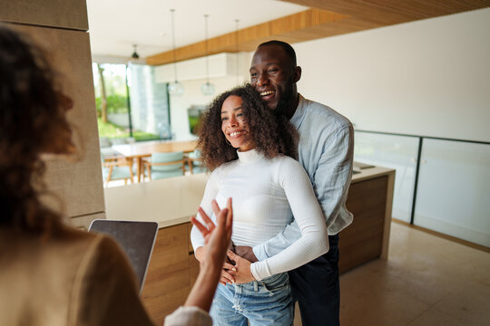 Professional female real estate agent in business attire demonstrates property details on tablet during consultation with diverse couple in modern office setting.
