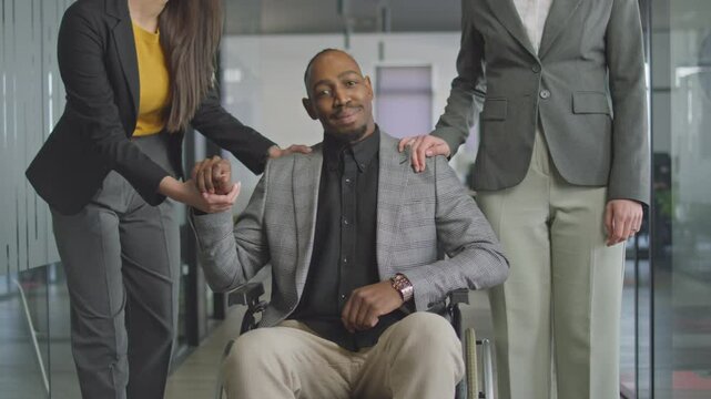 Diverse group of colleagues interacts with a man in a wheelchair in a modern office hallway, fostering an inclusive and supportive environment. Concept of teamwork and accessibility