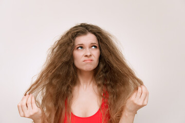 A young woman with voluminous, curly hair looks frustrated as she examines her dry, tangled...