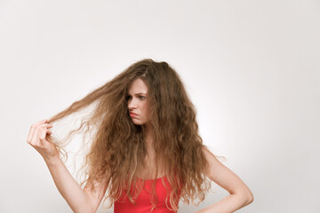 A young woman with voluminous, curly hair looks frustrated as she examines her dry, tangled strands.The struggle of maintaining unruly hair, highlighting beauty challenges and self-care. Bad hair day