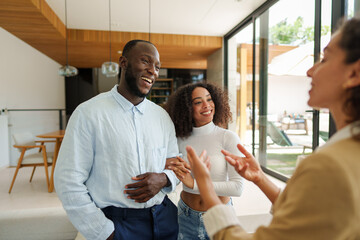 Diverse couple meets with real estate agent in modern home interior featuring wood accents and natural lighting during property consultation meeting.