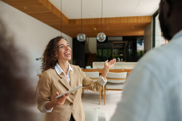 Caucasian female real estate professional in beige blazer enthusiastically discusses property...