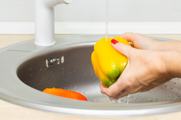 woman washing bell peppers in kitchen sink. housewife washes vegetables in the kitchen. bell pepper in the kitchen. yellow bell pepper.