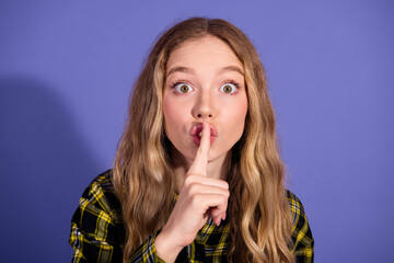 Naklejka premium Young woman showing silence gesture with finger on lips, wearing checkered shirt, purple background