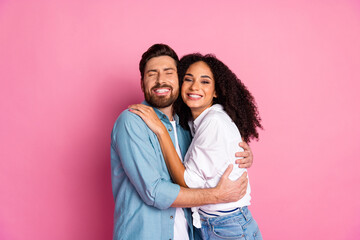 Happy multiethnic couple embracing and smiling against a pink background