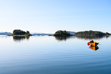 Panoramic view of a Norwegian fjord with small islands at the horizon and a wooden boat in front. The surface of the water is calm.