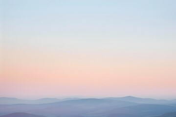 Soft pastel sunrise colors paint the sky above a range of hazy, bluetoned mountains. Peaceful and dreamy landscape.