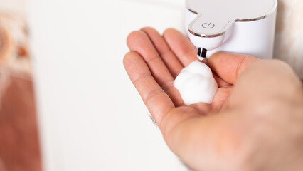 Hand pressing dispenser to obtain foamy soap in a bright bathroom setting during daytime