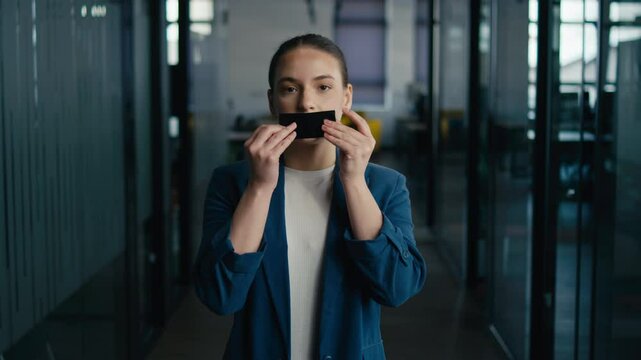 Young professional woman in a modern office, taping her mouth as a symbolic gesture of silence. Concept of censorship, restriction, or lack of freedom of speech in workplace settings.