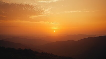 Obraz premium Stunning sunset over mountain range. Warm golden light illuminates the hazy landscape. Perfect for travel, nature, and serenity themes
