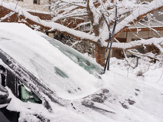 A cropped view of a car with the windshield cleared of snow, while the surrounding glass and roof remain covered in frost. The contrast highlights the effort of winter mornings, preparing the vehicle 