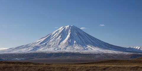Fototapeta premium A majestic snow-capped mountain rises proudly against a clear blue sky, showcasing the stunning beauty of nature and the power of geological formations.
