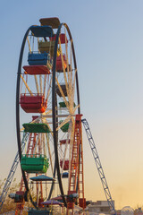 Fototapeta premium Colorful Ferris Wheel in the Evening Light. Classic Ferris Wheel with bright red, blue, green, and yellow cabins