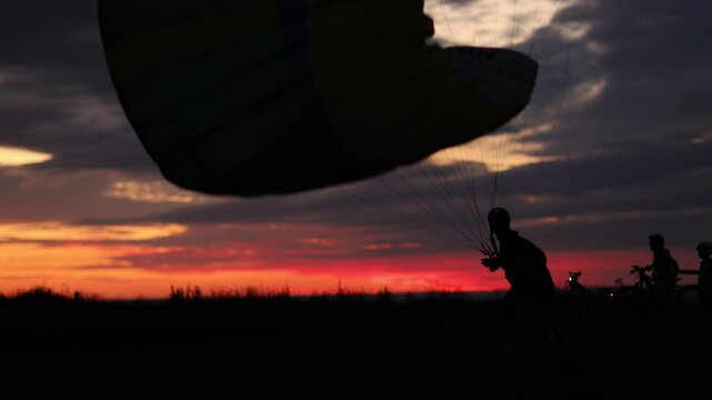 Lądujący paralotniarz na tle zachodzącego r&oacute;żowego  nieba