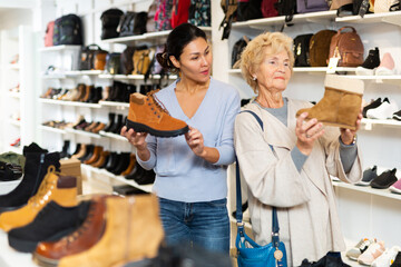Old lady choosing new shoes in shoeshop. Asian woman consulting her about footwear.