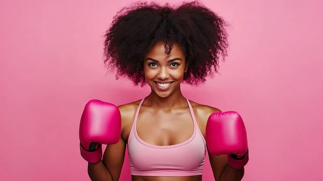 A confident young black woman displays her strength in pink boxing gloves while smiling against a matching backdrop, embodying empowerment and energy