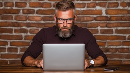 man with a beard wearing glasses intensely types on a laptop in an inviting workspace. background features rustic brick walls, creating a warm and creative atmosphere