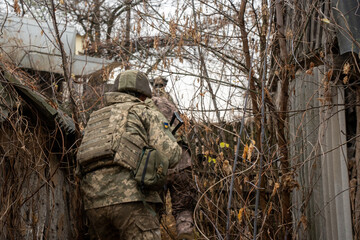 Group of Ukrainian infantry soldiers in camouflage gear advancing towards a brick building. The...