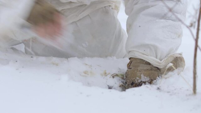Sapper soldier places an anti-personnel mine on a tripwire. Military sapper mines and camouflages a mine in snow. Soldier in a winter camouflage suit mines an area. Preventing enemy entering area