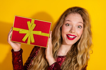 Young woman with a joyful expression holding a festive gift, dressed in red sequins against a vibrant yellow background