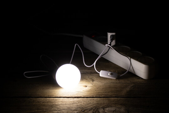 An energy-saving light bulb is on the wooden floor near the socket