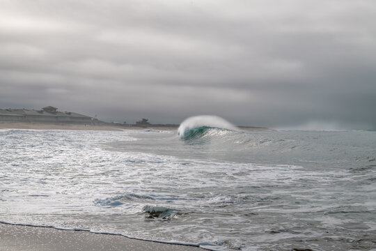 A breaking wave with spray forming a mane on an overcast day