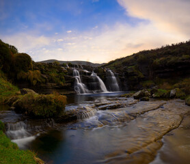 Waterfall with 3 water jets, which flows into a stream. At sunset in autumn