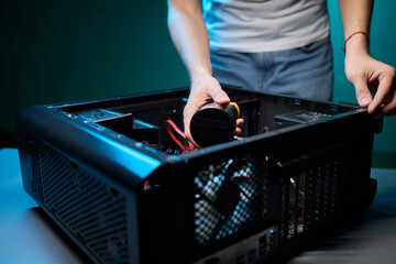 A man cleans a computer case with a vacuum in a bright room, stressing workspace tidiness