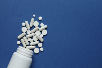 Various pills pouring out of medicine bottle on colorful background