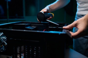 A man cleans a computer case with a vacuum in a bright room, stressing workspace tidiness