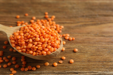 Red lentils in spoon on wooden background 
