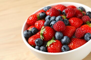 Different fresh ripe berries in bowl on wooden table