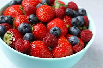 Different fresh ripe berries in bowl on gray table
