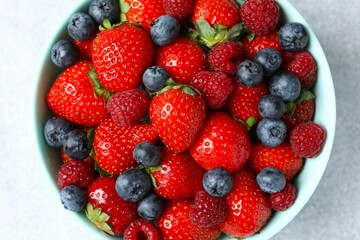 Different fresh ripe berries in bowl on gray table