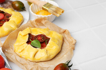 Raw galettes with tomato and basil on white tiled table, closeup. Space for text