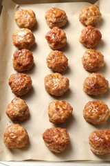 Many delicious meatballs on parchment in baking dish, above view