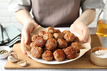 Woman holding plate with delicious meatballs at light textured table, closeup