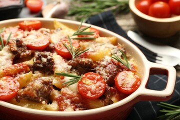 Delicious pasta casserole with cheese, tomatoes, minced meat and rosemary in baking dish on table, closeup