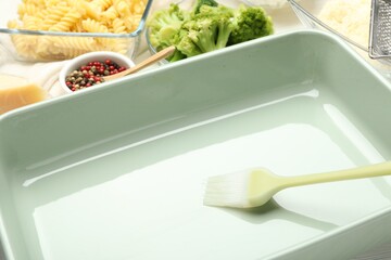 Ceramic casserole, brush and ingredients on table, closeup