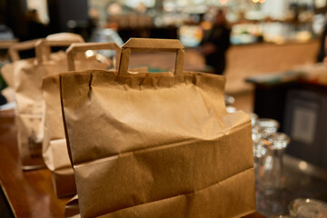 There are three craft paper bags placed neatly on a rustic wooden counter inside a cafe setting
