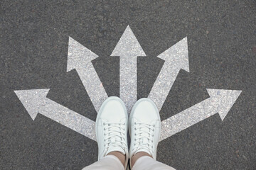 Woman standing on asphalt road with white arrows pointing in different directions, top view....