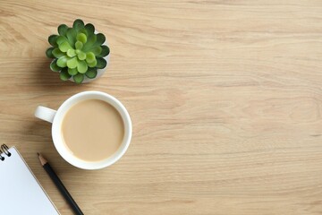 Office table with notebook, pencil, green plant and cup of coffee, top view
