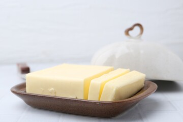 Cut tasty butter in dish on white table, closeup