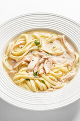 chicken noodle soup with herbs in a white bowl