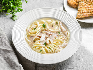 chicken noodle soup with herbs in a white bowl