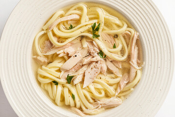 chicken noodle soup with herbs in a white bowl