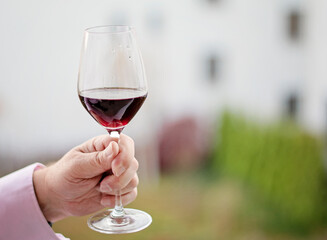 Half full glass of red wine in human hand. Person holding a glass of wine. Copy space, space for text. Tasting expensive wine.