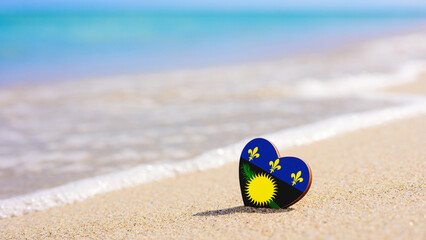 Obraz premium Flag of Guadeloupe in the shape of a heart on a sandy beach.