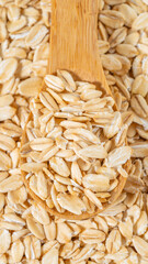 Raw rolled oats in a wooden spoon on a bed of oats, showcasing natural texture, whole grains, and healthy food concept.